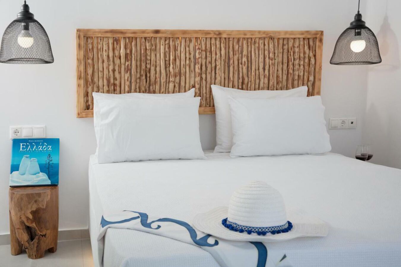 A neatly made bed with white bedding and pillows, a wooden headboard, and two black pendant lights.