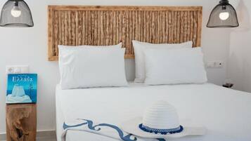 A neatly made bed with white bedding and pillows, a wooden headboard, and two black pendant lights.