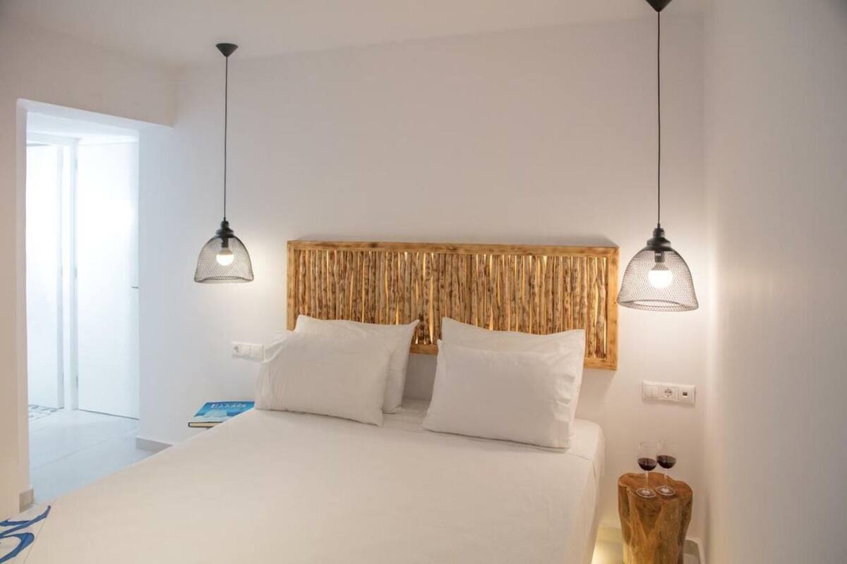 Een slaapkamer met een bed, twee hanglampen, een houten hoofdeinde en een nachtkastje met twee wijnglazen.