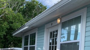 A wooden deck with white railings leading to a light blue house with a white door and windows.