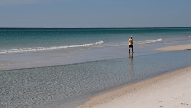 A beach with clear water and a person standing in the shallow water.