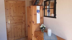 Une porte en bois, un meuble en bois avec un calendrier, une petite table sur laquelle se trouvent un vase et une bougie, et un miroir fixé au mur.