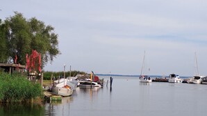 Un port de plaisance où sont amarrés plusieurs bateaux, une structure en bois ornée de drapeaux rouges et une étendue d’eau calme.