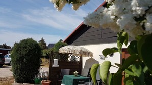 Un espace extérieur aménagé avec une table et des chaises, un coin salon abrité et un bâtiment portant une enseigne.