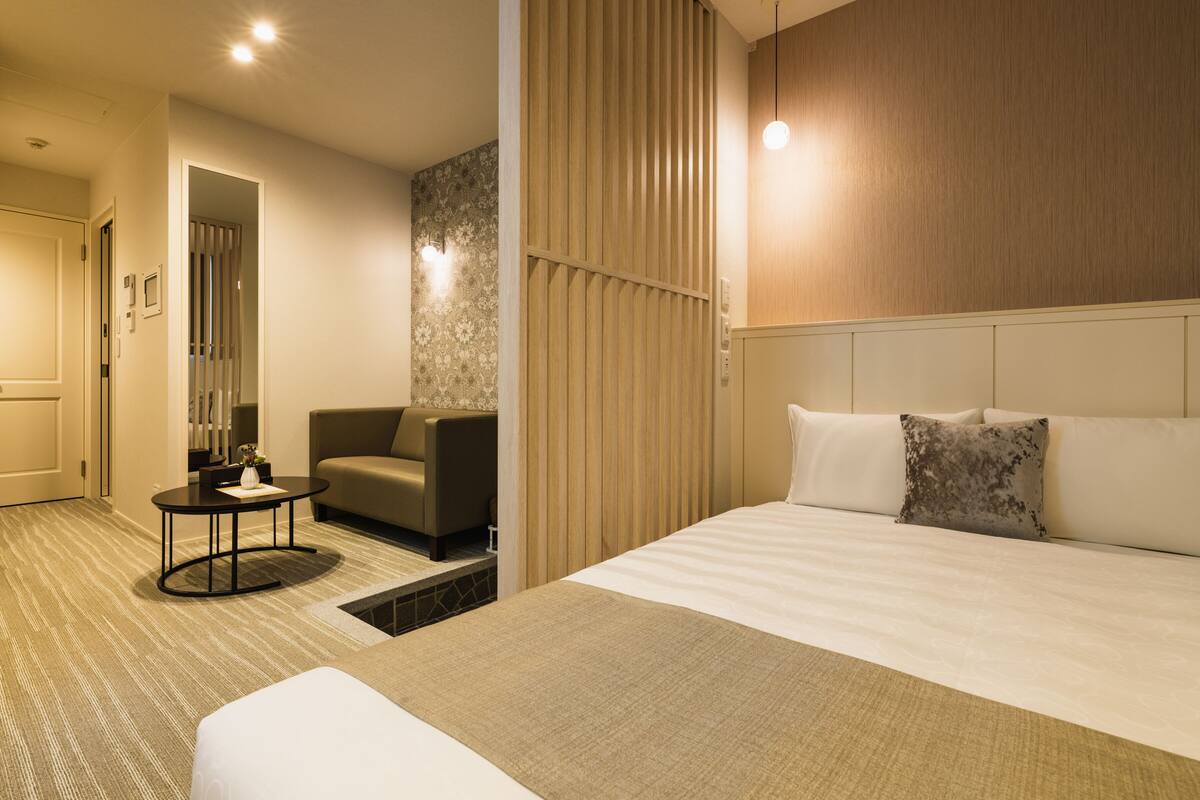 Ein Hotelzimmer mit Bett, einer Couch, einem kleinen Tisch und einer Wand mit vertikalen Jalousien.