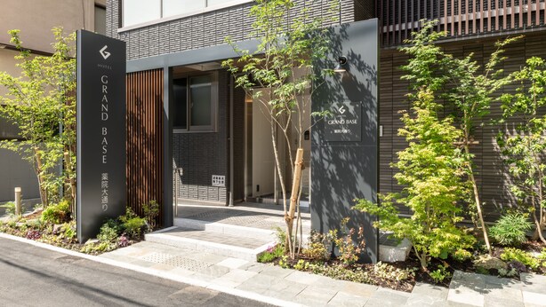 Une entrée d’hôtel moderne avec une enseigne indiquant « GRAND BASE » et « HÔTEL GRAND BASE ».
