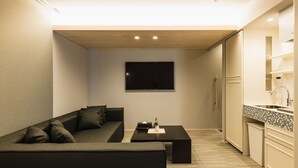 Un espace de vie compact comprenant un canapé, une table basse, un téléviseur à écran plat et une kitchenette.