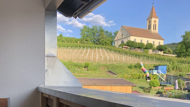 A balcony with a view of a church and vineyard. - Ferien auf Rüdlins Winzerhof (Auggen)