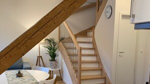 A dining area with a wooden staircase, a dining table with chairs, and a potted plant. - Ferien auf Rüdlins Winzerhof (Auggen)