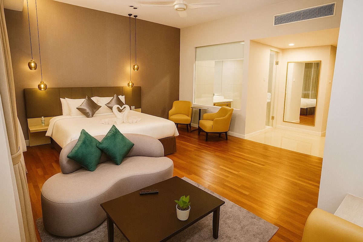 A modern hotel room with a large bed, two armchairs, a small table, and a potted plant.