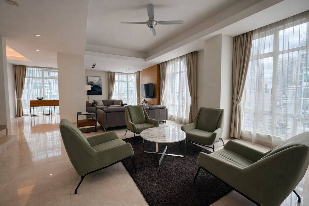A modern living room with a round coffee table, green armchairs, a sofa, and a dining area with a bench.