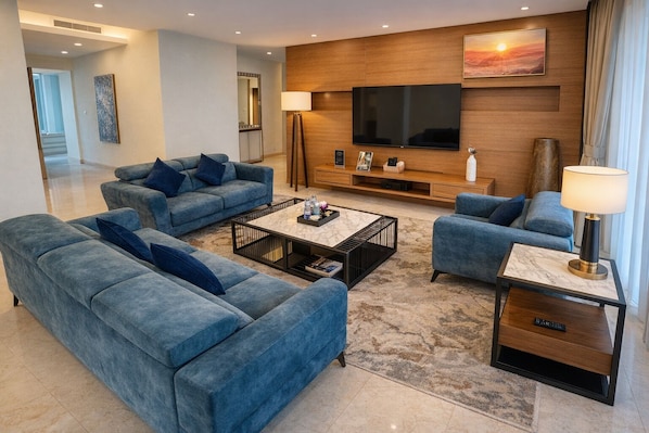 A modern living room with a large flat-screen TV, blue sofas, a coffee table, and a lamp. - Cormar Suites Kuala Lumpur (Kuala Lumpur)