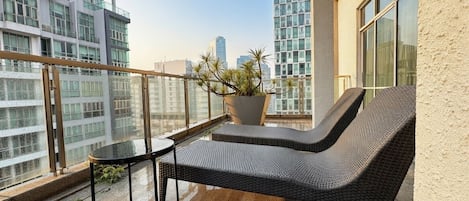 Ein Balkon mit einer Korbsitzgruppe, einem kleinen Tisch, einer Topfpflanze und Blick auf die Stadt.