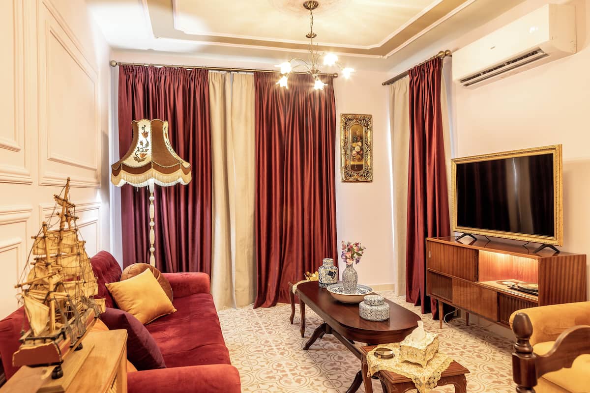 A well-furnished living room with a red sofa, a wooden coffee table, a ship model, a lamp, and a television.