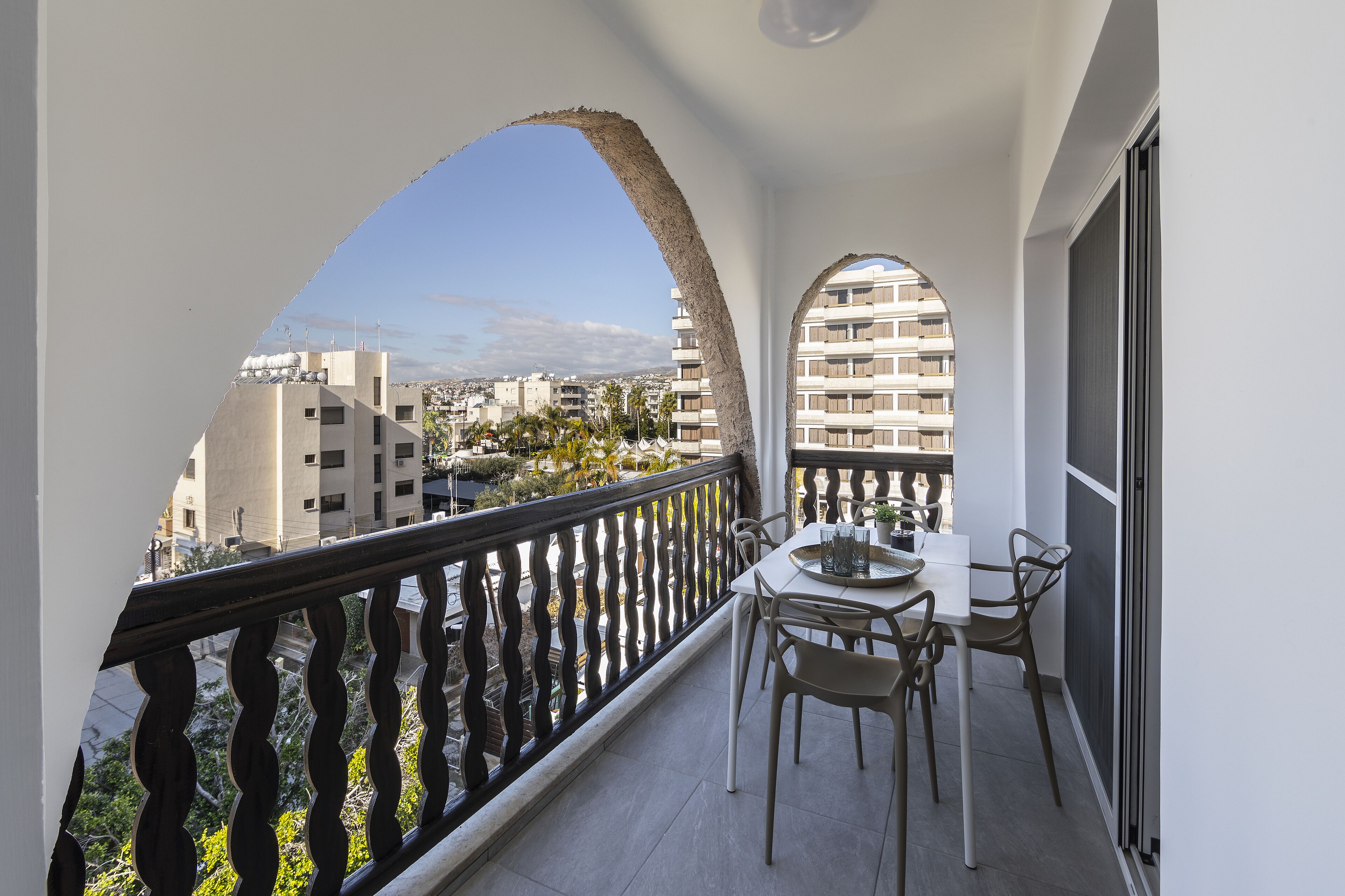 A balcony with a table and chairs, a view of a cityscape, and a railing.