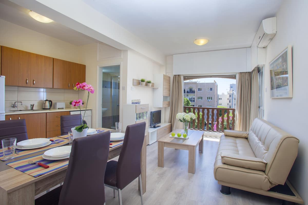 A modern apartment with a dining area, a sofa, and a balcony with a view of buildings.