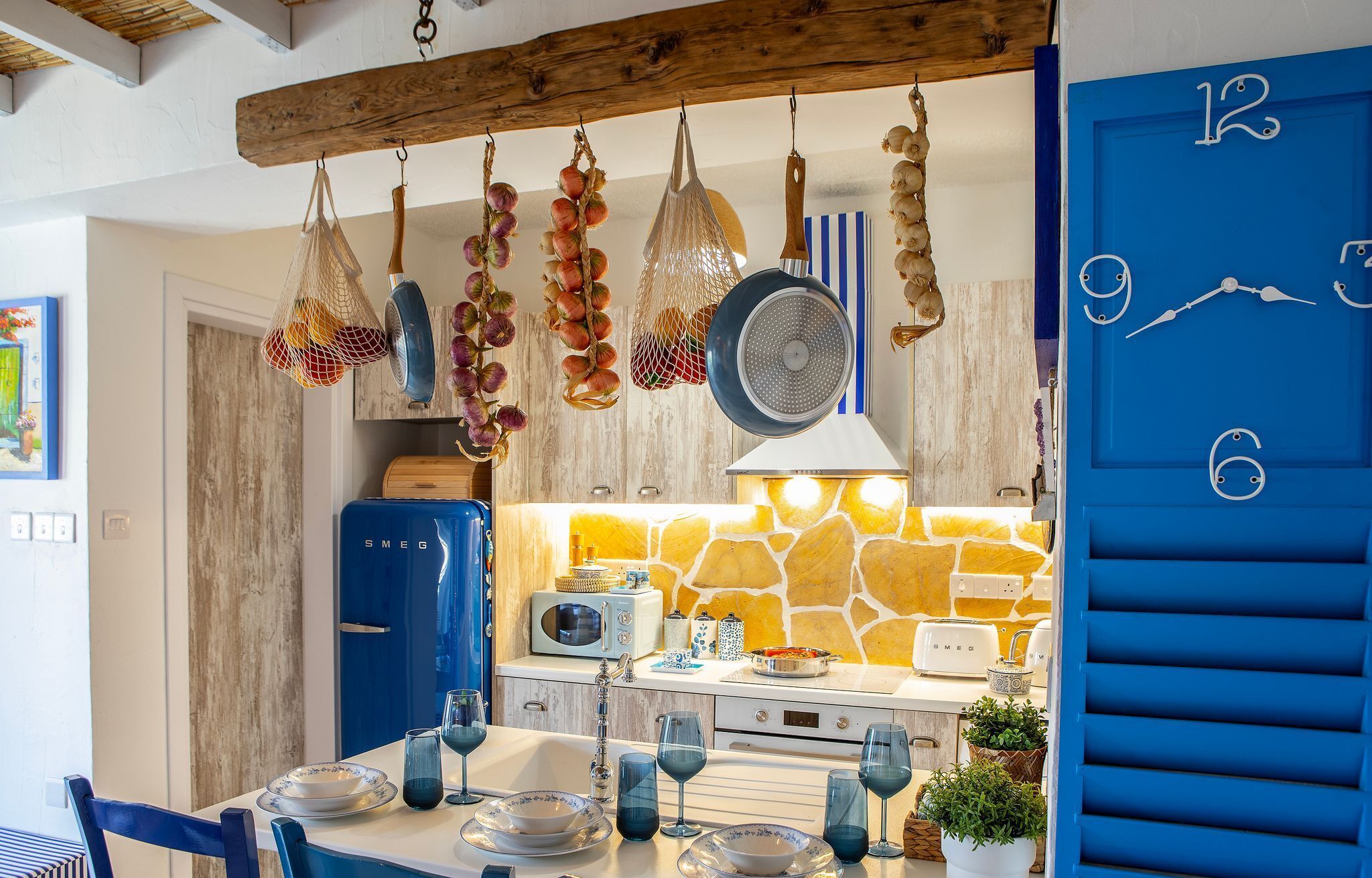 A kitchen with hanging garlic, a blue door with numbers, and a stone wall backsplash.