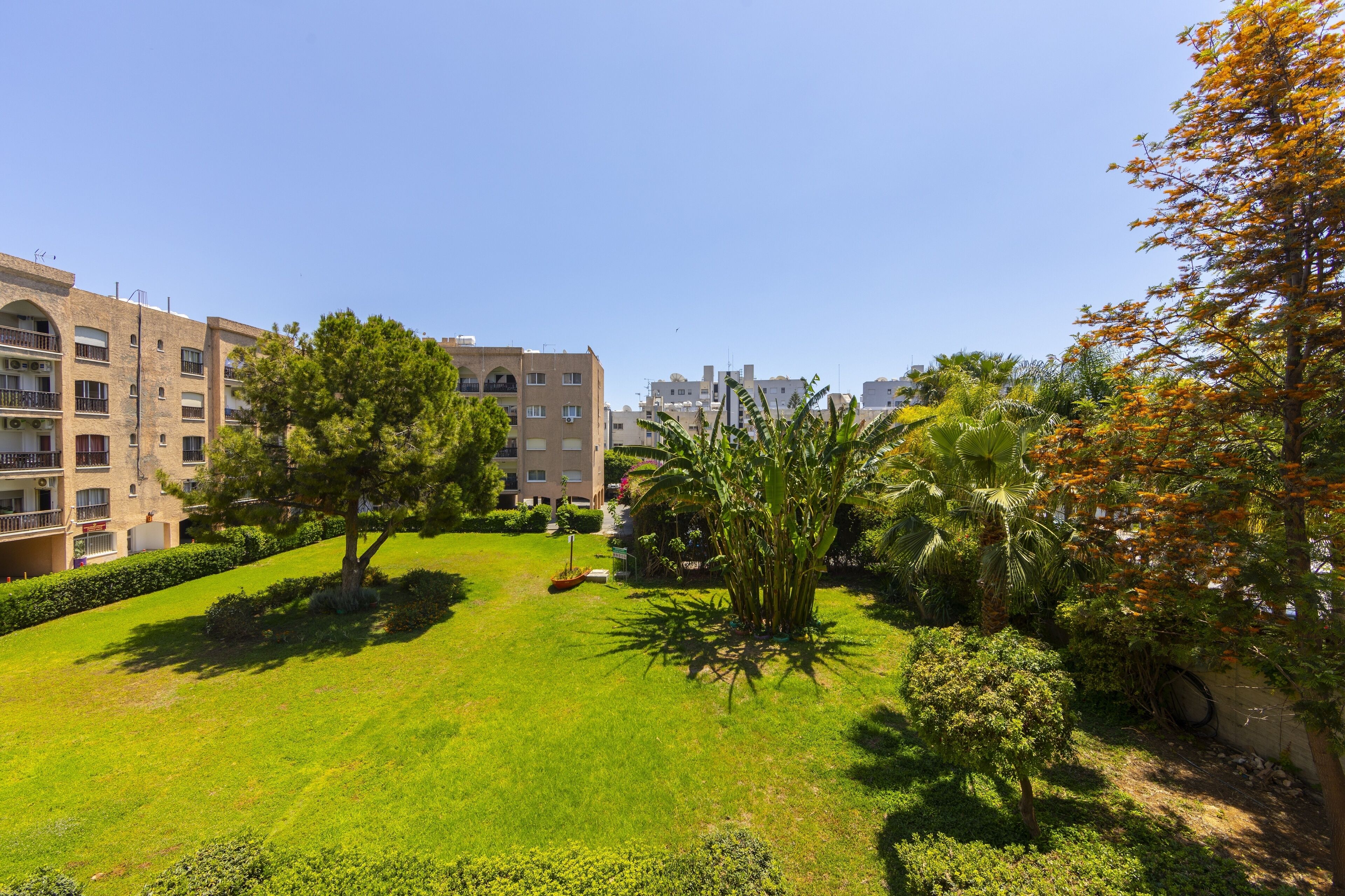 A well-maintained courtyard with a lawn, trees, and a building with multiple balconies.