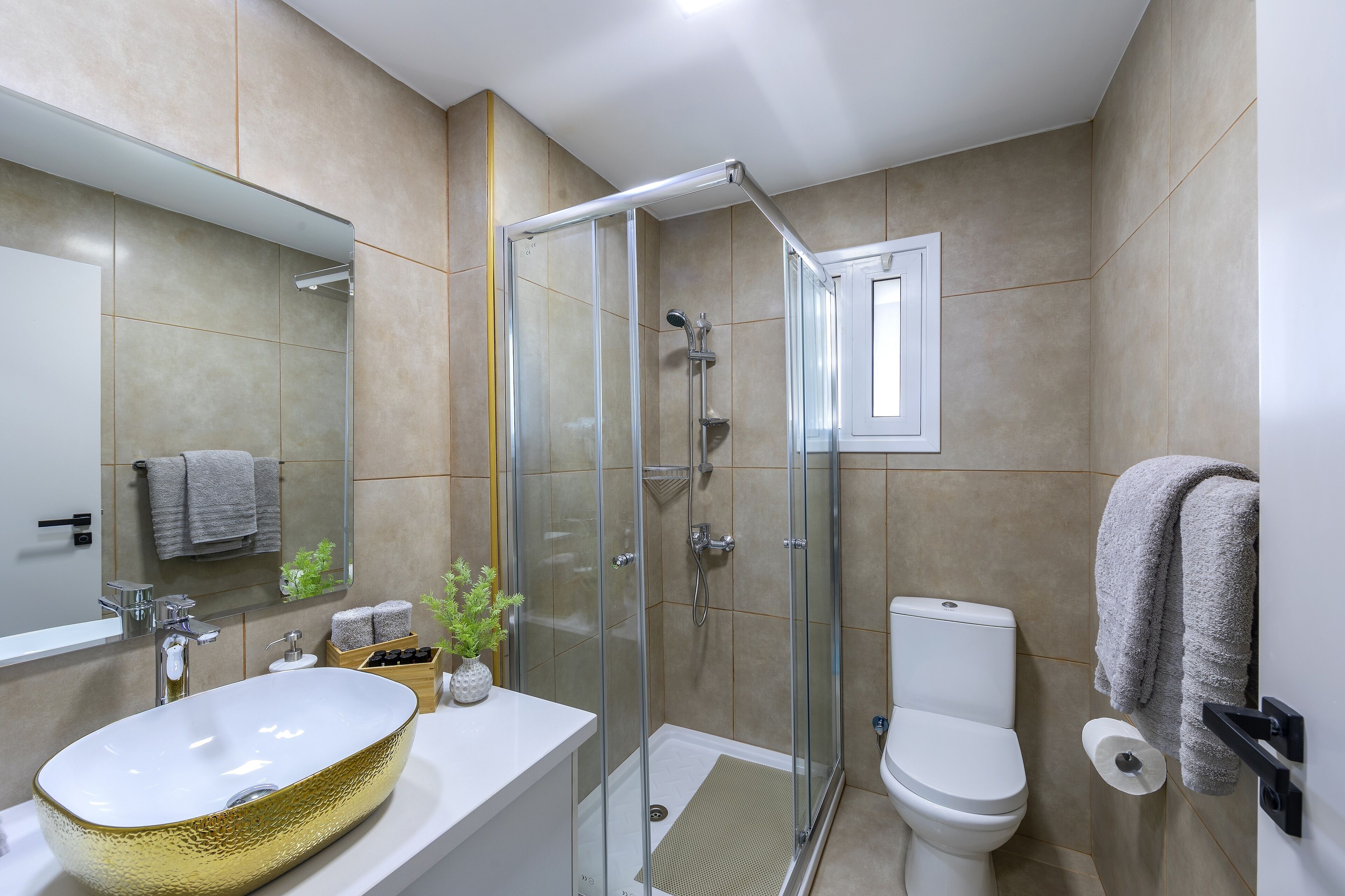 A modern bathroom with a glass-enclosed shower, a white sink with a gold basin, a toilet, and a towel rack.