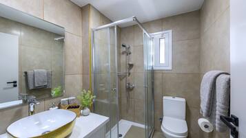 A modern bathroom with a glass-enclosed shower, a white sink with a gold basin, a toilet, and a towel rack.