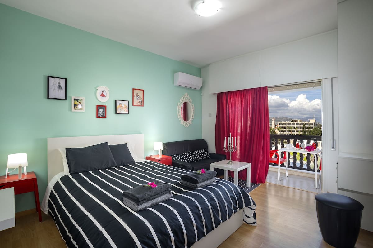 A hotel room with a bed, a nightstand, a small table, a window with a view, and a balcony.