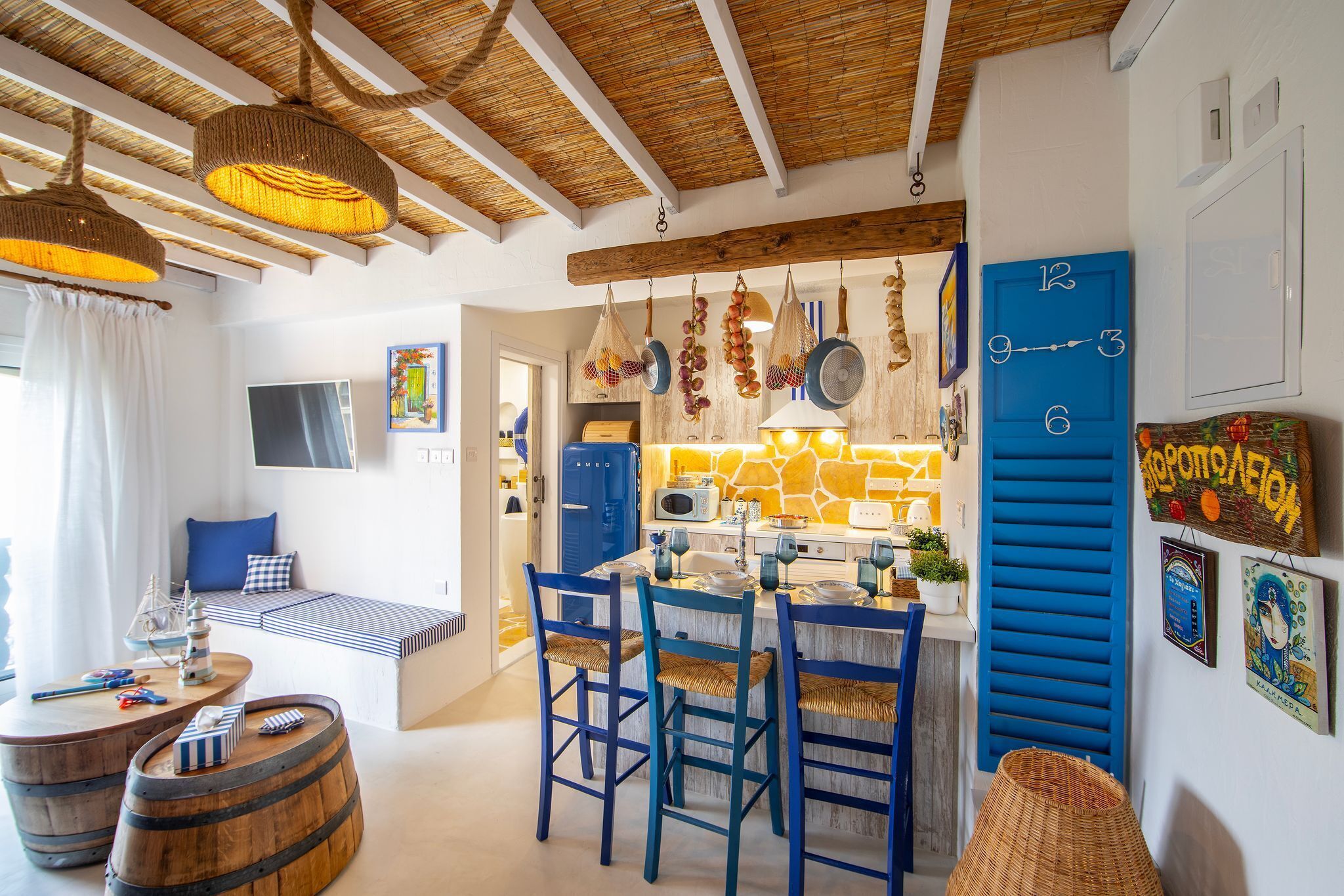 Une cuisine chaleureuse avec une horloge bleue, des poutres en bois au plafond et un coin repas avec des chaises bleues.