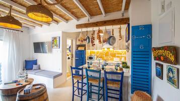 Une cuisine chaleureuse avec une horloge bleue, des poutres en bois au plafond et un coin repas avec des chaises bleues.