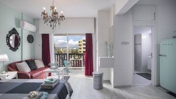 Une chambre d’hôtel moderne avec un lit, un canapé en cuir rouge, un lustre et un balcon agrémenté de rideaux rouges.