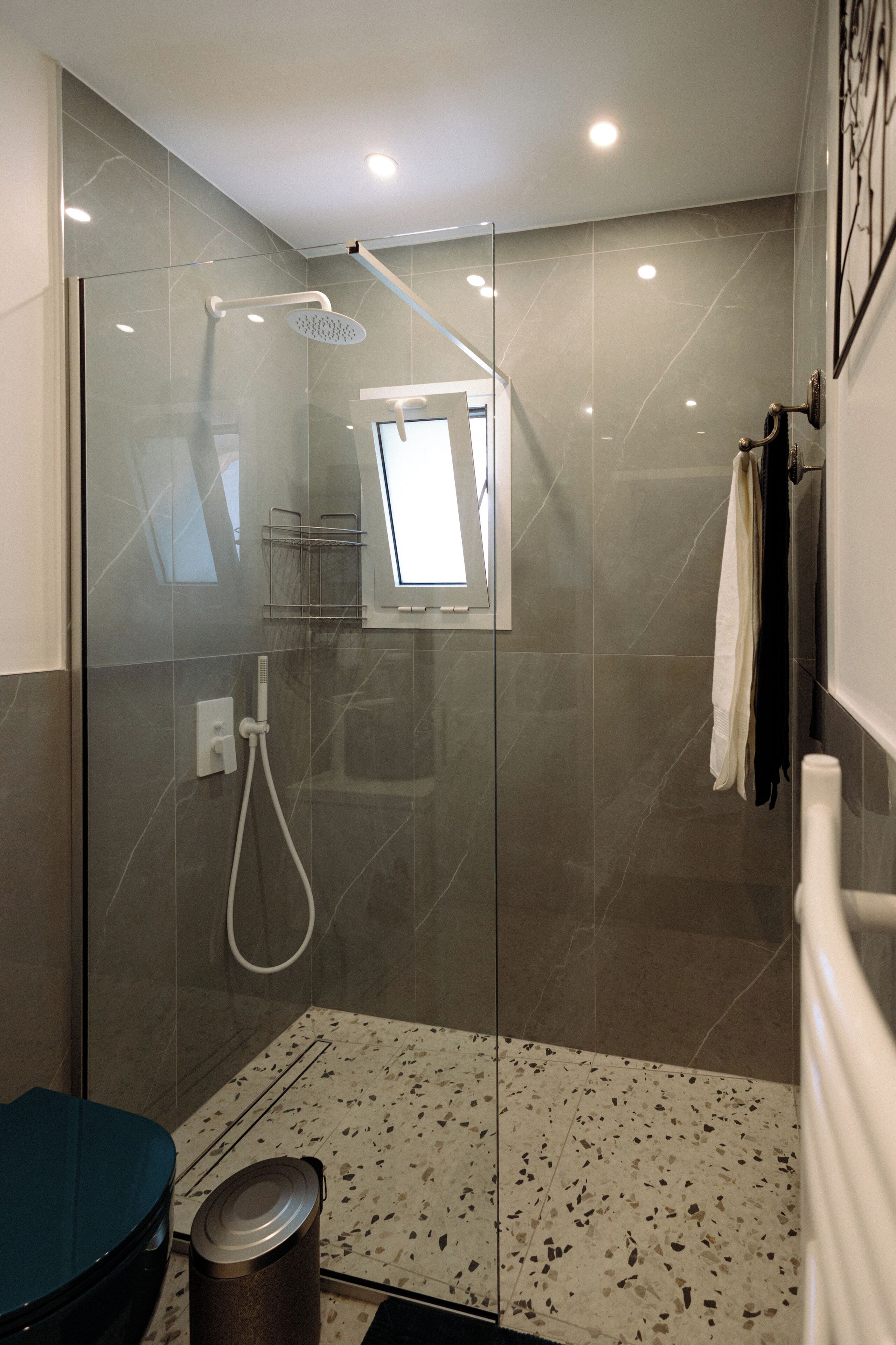 A modern shower with a glass door, a small window, and a towel rack.