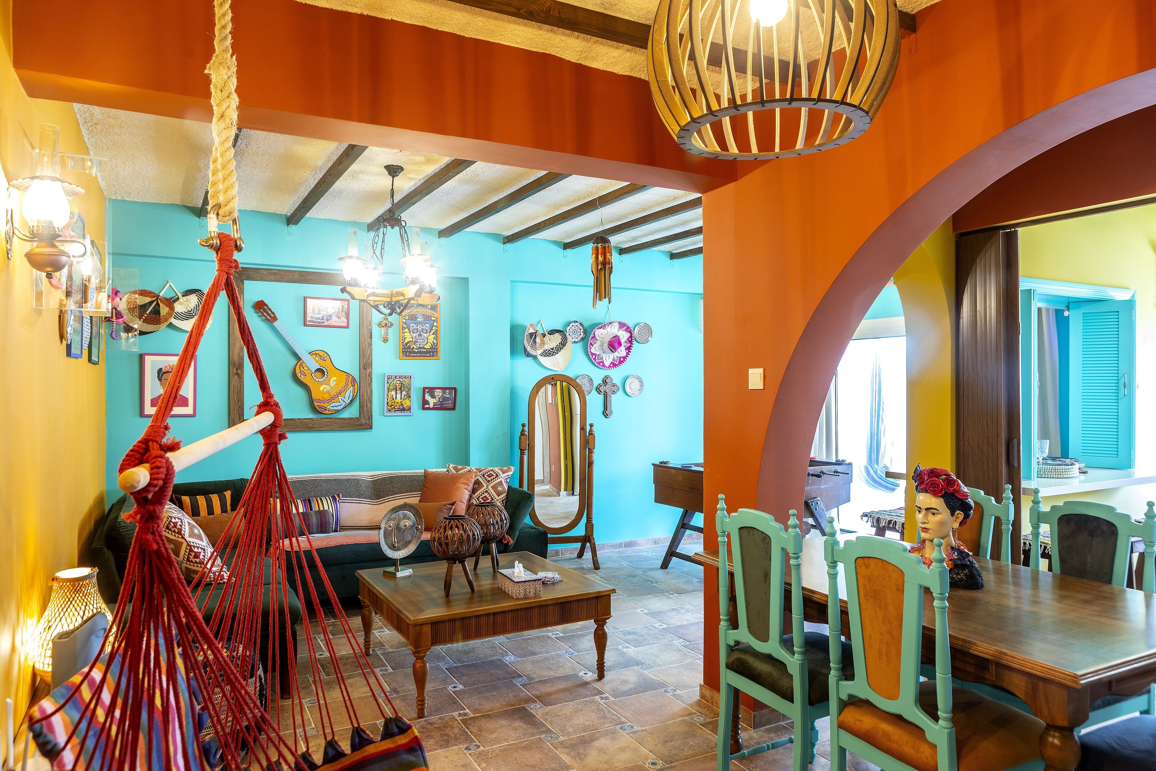 Un salon chaleureux avec un hamac, un coin repas avec des chaises et un grand miroir au mur.