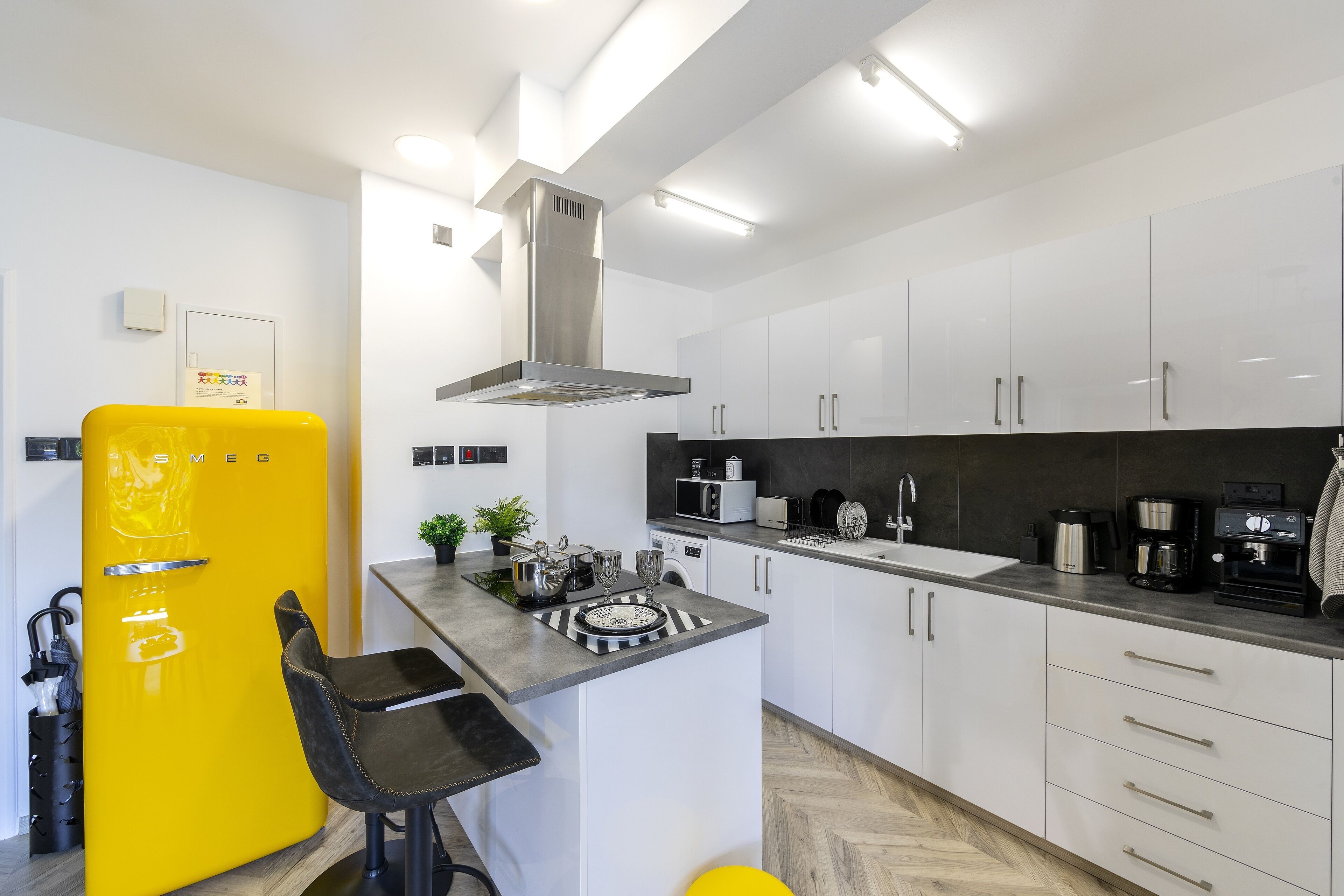 A modern kitchen with white cabinets, a stainless steel range hood, and a yellow refrigerator.