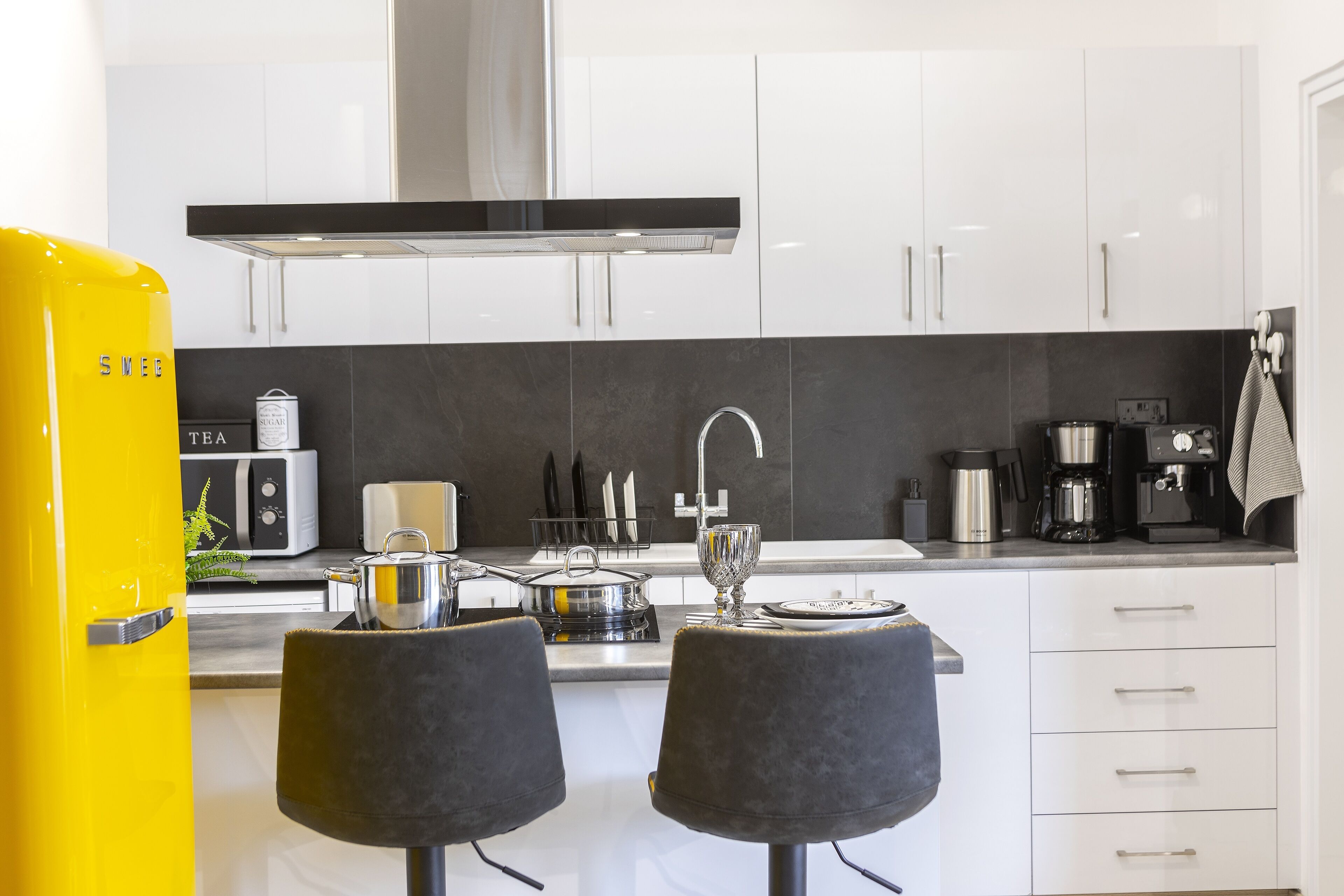 A modern kitchen with white cabinets, a black countertop, and a yellow appliance.