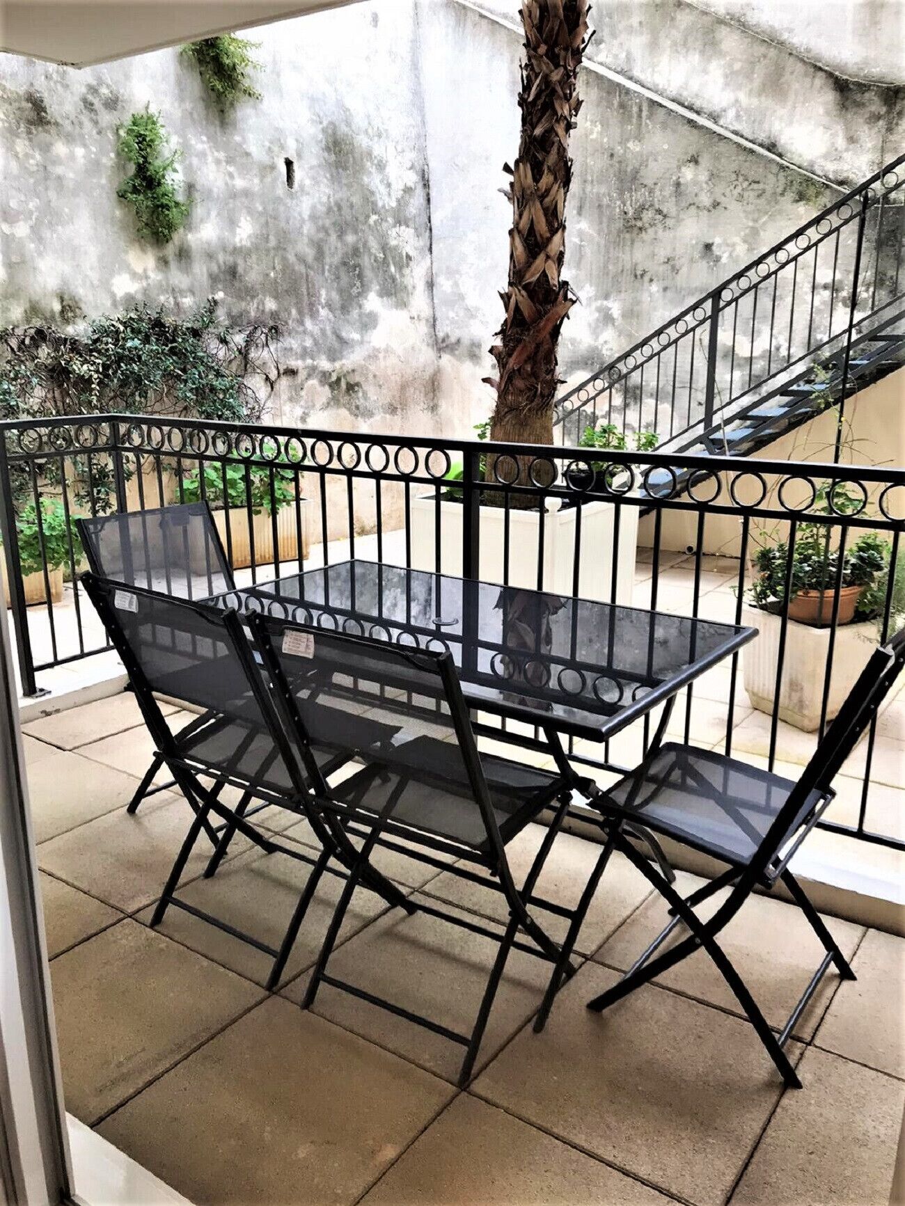 Un'area patio con tavolo e sedie, una scala e un muro in cemento decorato con piante.