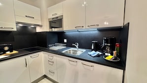 A modern kitchen with white cabinets, a black countertop, stainless steel sink, and a coffee maker.