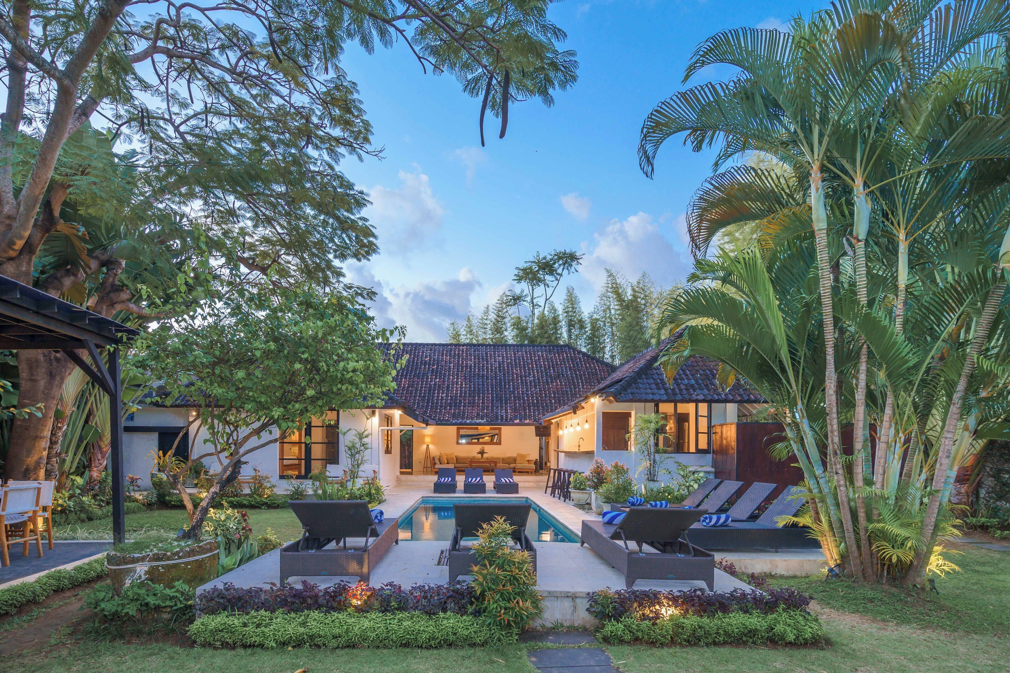 A modern house with a swimming pool, outdoor seating, and lush greenery.