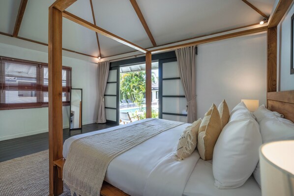 A bedroom with a large bed, wooden beams, a view of a pool, and a balcony.