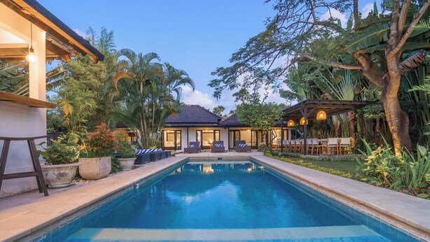 A swimming pool with lounge chairs and a covered seating area, surrounded by tropical plants. - The Aryana Estate (Seminyak)