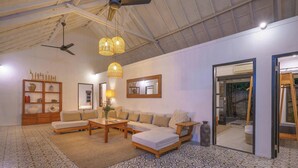 A spacious living room with a high ceiling, a ceiling fan, a sofa set, a coffee table, and a patterned floor. - The Aryana Estate (Seminyak)