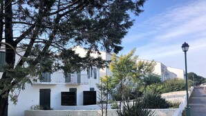 Un edificio blanco con balcones, un hidrante rojo y plantas verdes al frente.