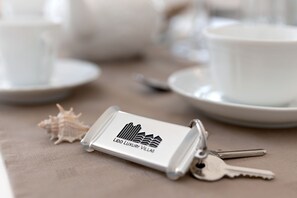A keychain with a hotel logo, keys, a seashell, and a cup on a table. - Villa Maestrale (Camaiore)