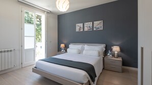 Un dormitorio con cama, mesitas de noche, un radiador y una puerta que da a un balcón.