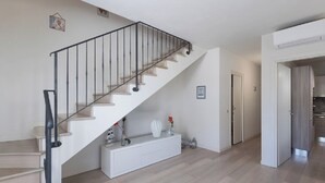 Una escalera con barandilla de metal, una consola blanca con objetos decorativos y una puerta que da a una cocina.