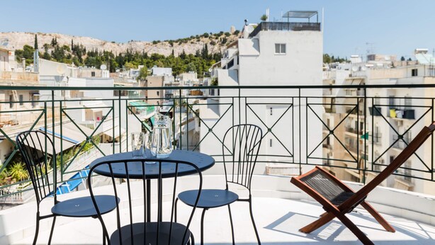 Een balkon met een tafel en stoelen, met uitzicht op een stadsbeeld met gebouwen en een heuvel.