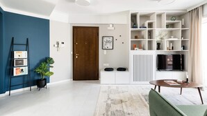 Een moderne woonkamer met een blauwe accentmuur, een houten deur, een witte console en een televisietoestel, plus een boekenkast.