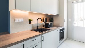 Een moderne keuken met een houten aanrecht, een zwart spoelbekken, een fornuis en witte kastjes.