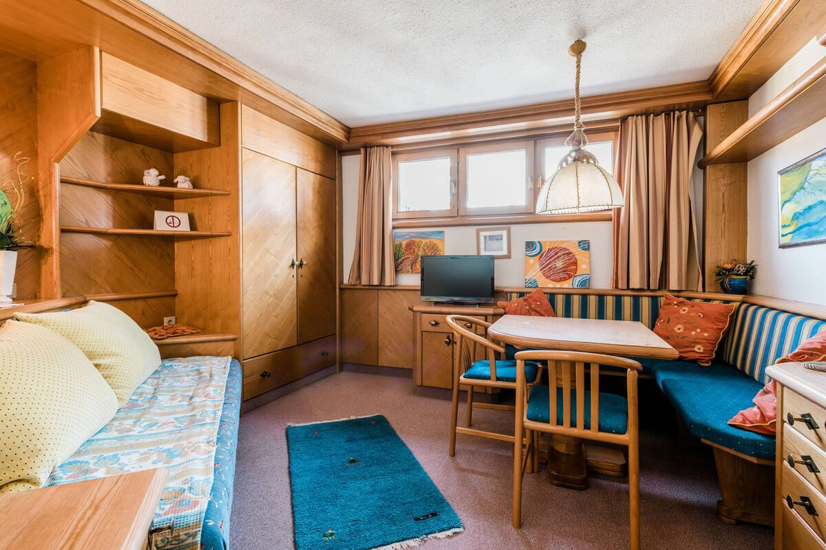 Espaço compacto para viver, com sofá, mesa pequena, televisão e janela com cortinas.