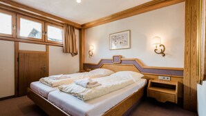 A bedroom with a wooden bed, two bedside tables, a nightstand, and a window with curtains. - Appartement Christine by Skinetworks (Sankt Anton am Arlberg)
