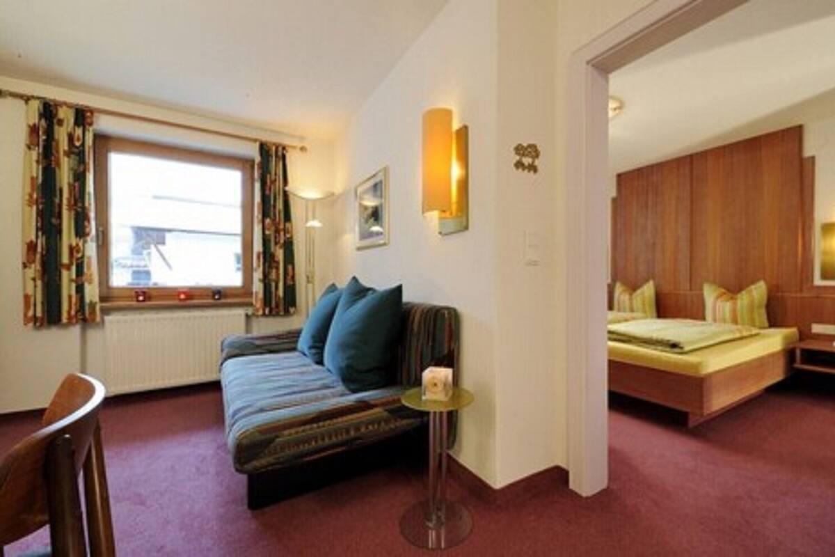 Quarto de hotel com sofá, mesa pequena, cama e janela com cortinas.