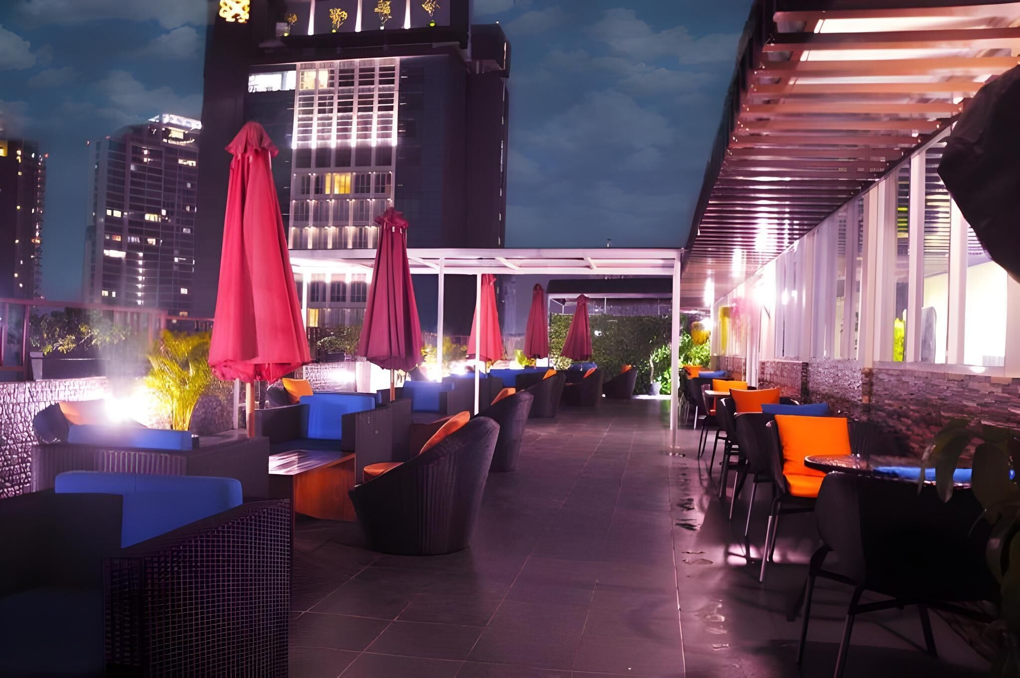 An outdoor seating area with tables and chairs, umbrellas, and a cityscape view in the background.