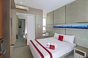 A hotel room with a large bed, a bedside table, a wall-mounted artwork, and a view of the hallway.